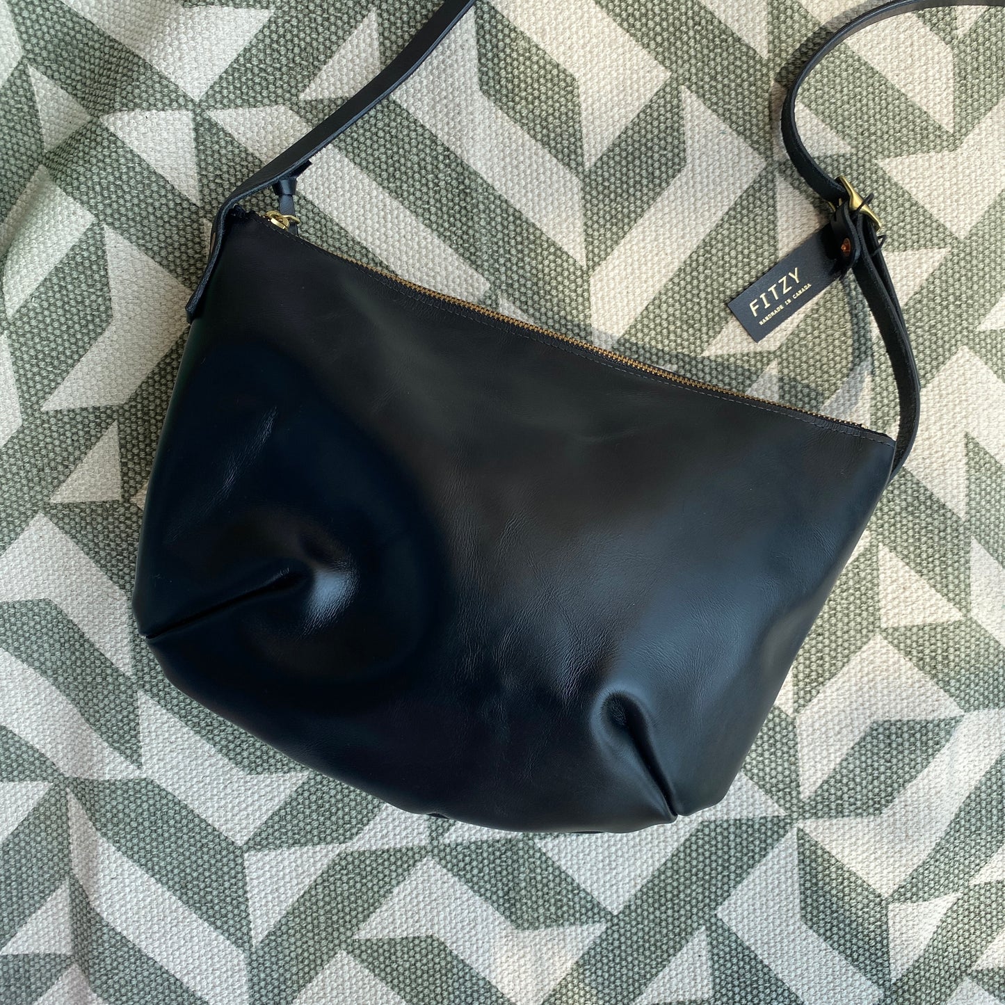 A black leather crossbody bag placed on a patterned surface.