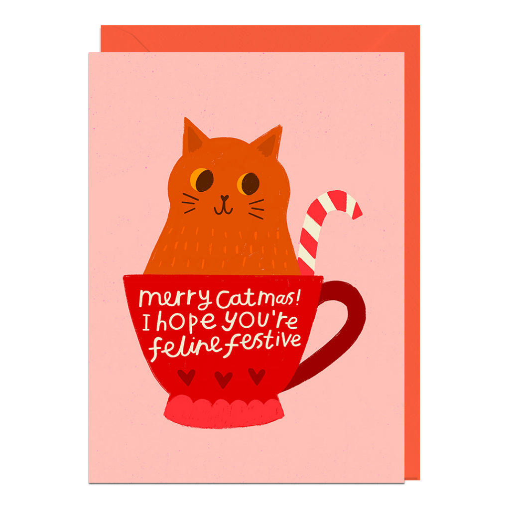Greeting card with a cat in a red mug and candy cane, on a pink background.