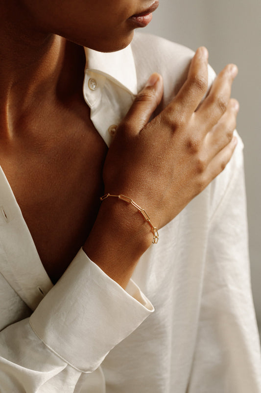 A person wearing a white shirt is showcasing a gold-colored bracelet on their wrist.
