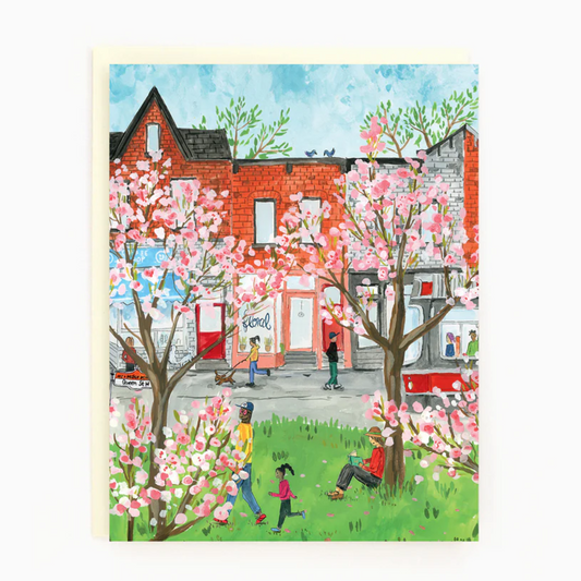 A colorful illustration of people walking on a street with cherry blossoms, a red building, and a blue sky background. The card is blank inside for a personal message.
