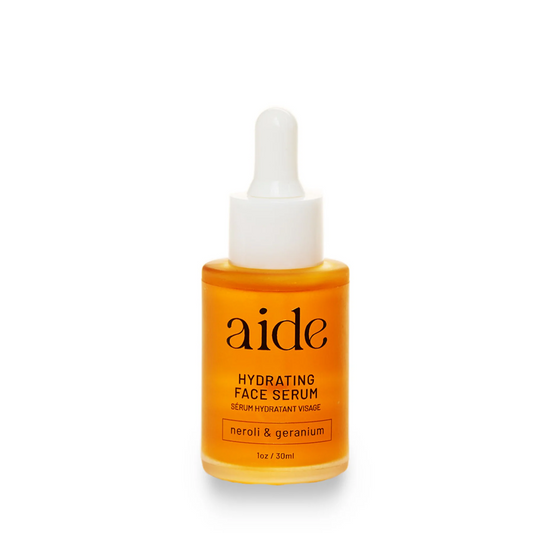 A glass bottle with a white dropper containing orange-colored hyaluronic acid serum, labeled 'aide HYDRATING FACE SERUM neroli & geranium'.