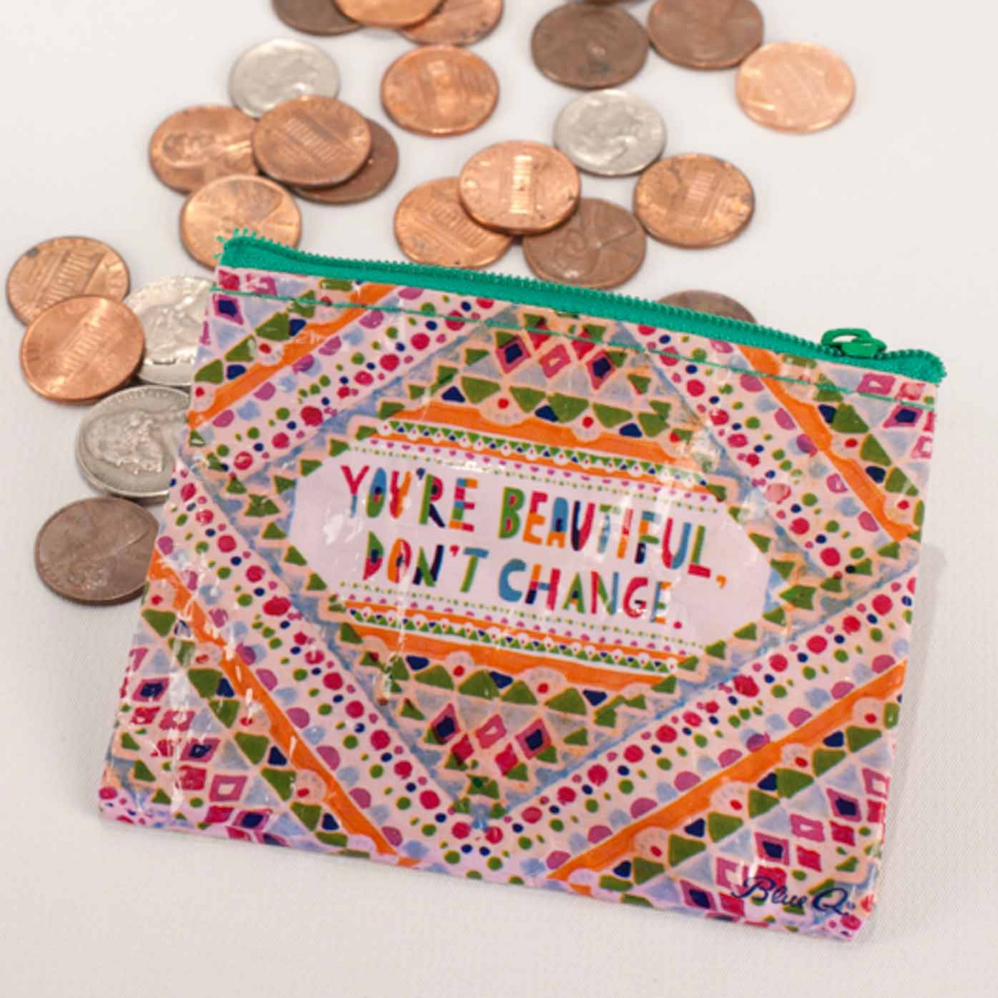 A multicolored geometric patterned coin purse with text 'YOU'RE BEAUTIFUL. DON'T CHANGE.' spread out with coins around it.