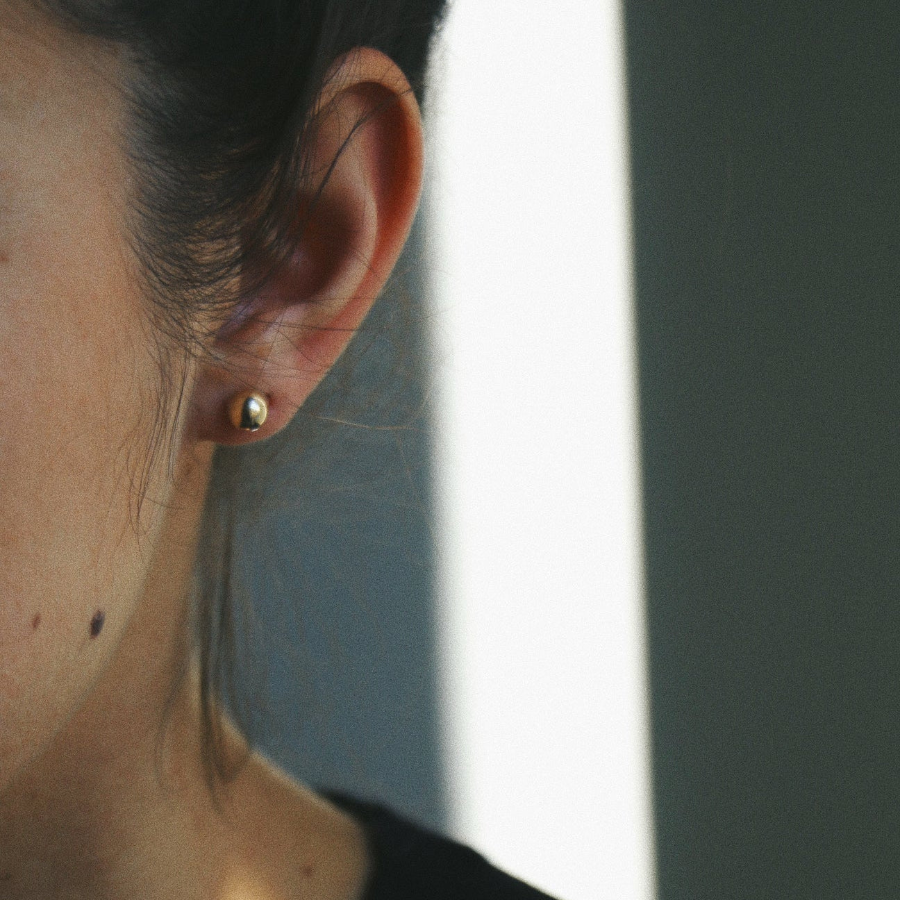 Close-up of an ear with a gold earring against a neutral background