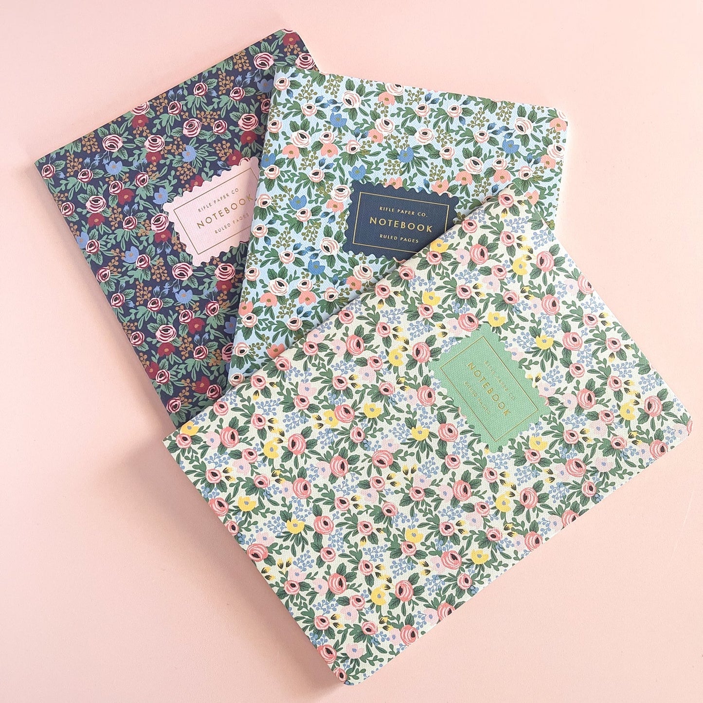 Three floral-patterned notebooks on a pink background