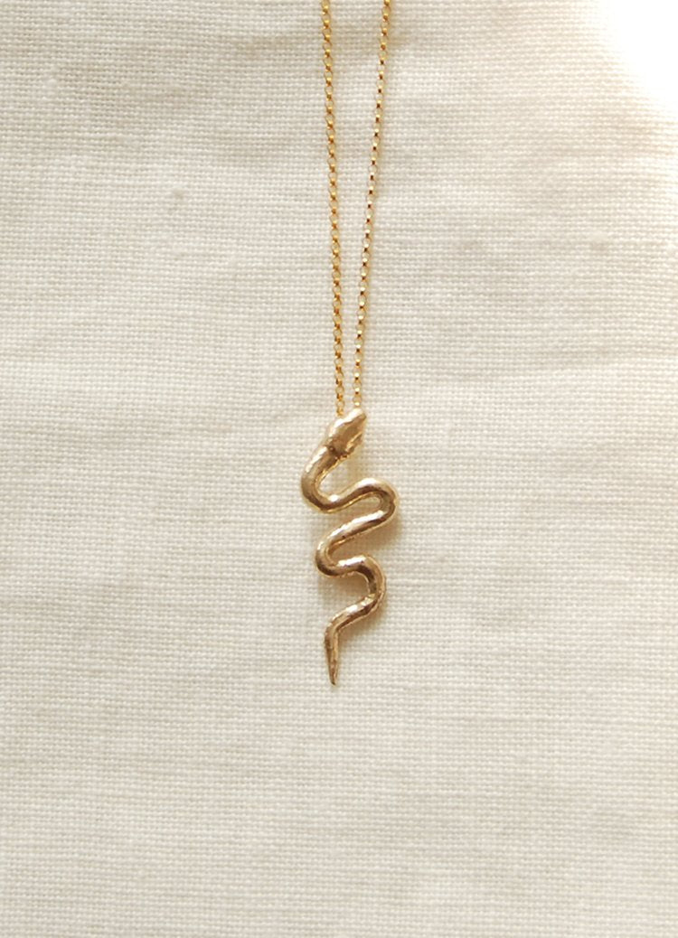 Gold snake-shaped pendant necklace on a beige fabric background